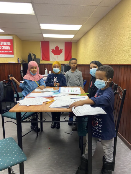 Five young students gathered around a table with their worksheets