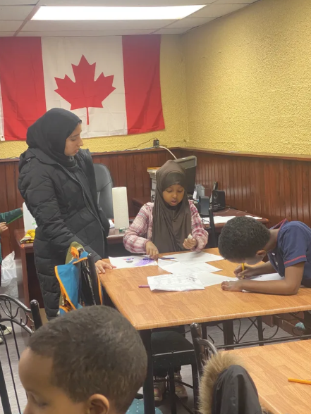 Adult mentor supporting children as they complete written activities