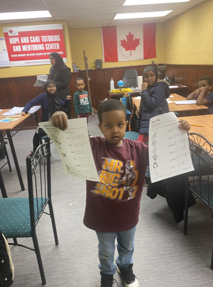 Young student proudly holding completed worksheets during a tutoring session